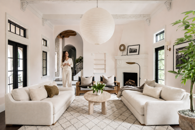 Bright neutral living room with cream sofas, a large paper lantern light, and a woman standing proudly in the background.