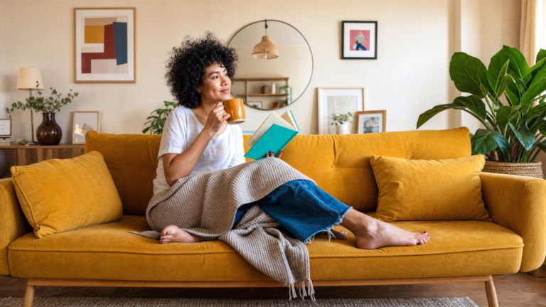 Woman relaxing on a cozy yellow sofa with a book and warm mug cozy gifts for her